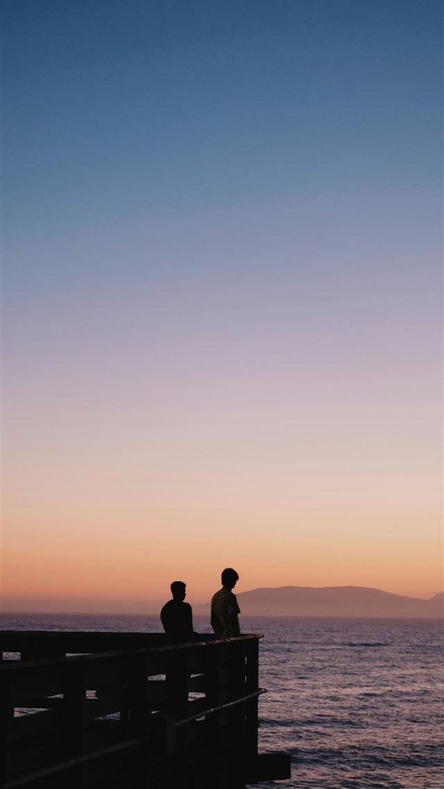 1290x2796 a couple of people sitting on top of a pier - portrait iPhone Wallpaper