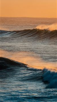 Ocean waves at sunset with warm orange sky wallpaper