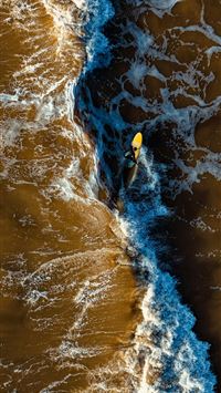 Surfer paddling on a yellow surfboard in brown oce... wallpaper