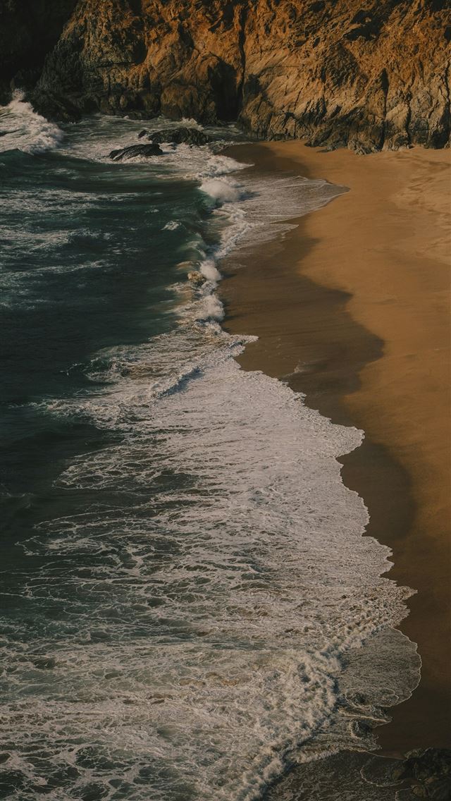 1290x2796 Waves crash on a sandy beach next to cliffs  -  iPhone Wallpaper