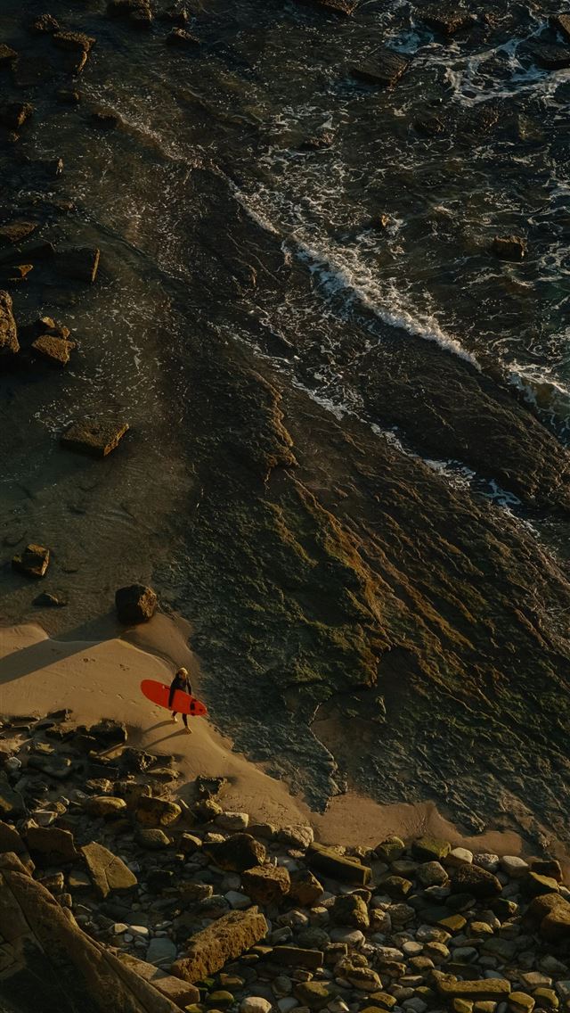 1290x2796 a red surfboard sitting on top of a rocky beach -  iPhone Wallpaper