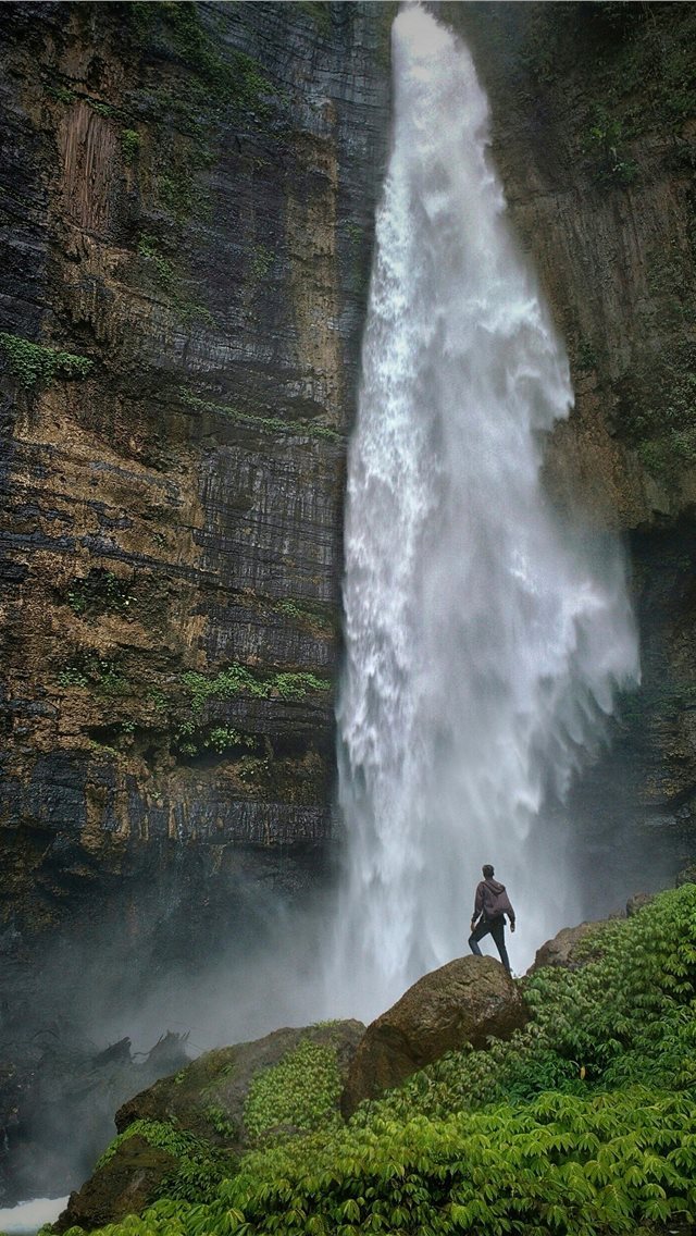 640x1136 person standing on brown rock formation looking at... - waterfall iPhone Wallpaper