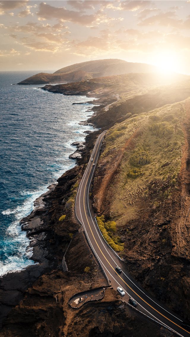 vehicles passing on road beside body of water duri... iPhone wallpaper 