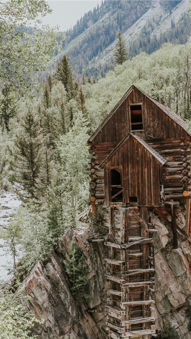 brown wooden house on rock formation near green tr... iPhone wallpaper 