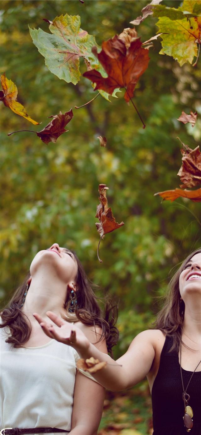 1125x2436 photo of two women throwing leaves during daytime - united states iPhone X Wallpaper
