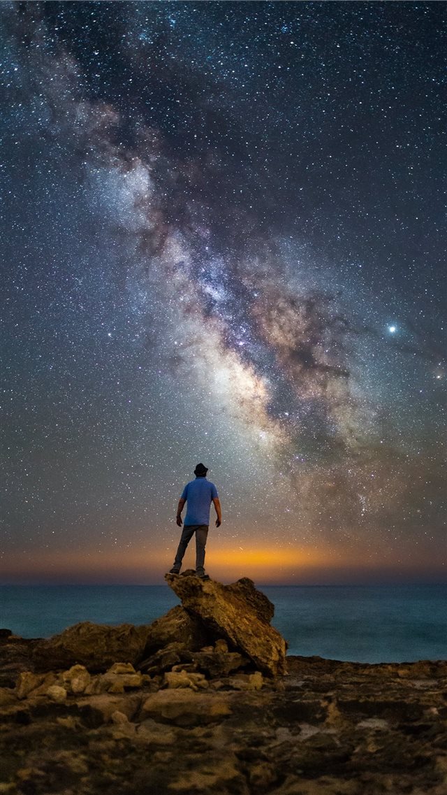 man standing on rock facing ocean under starry nig... iPhone 8 wallpaper 