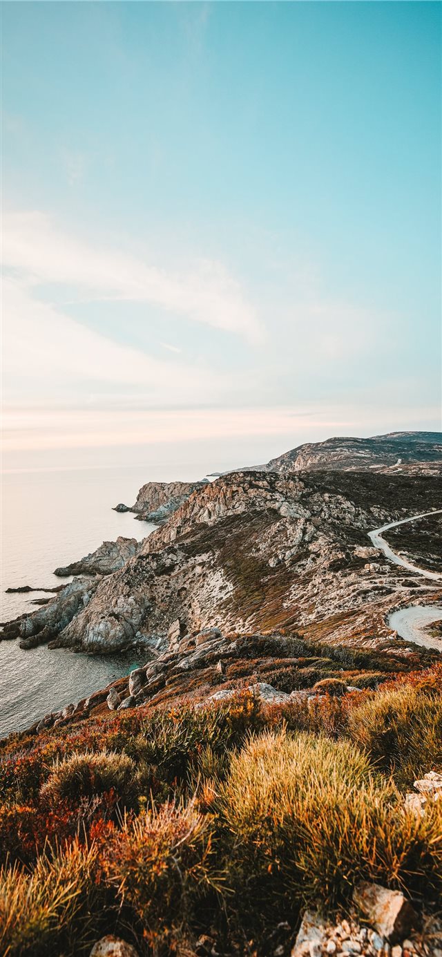 rocky cliff facing ocean under blue sky iPhone X wallpaper 
