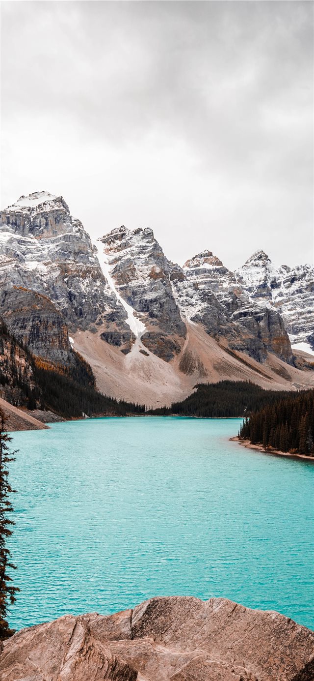 body of water near trees and glacier mountains dur... iPhone X wallpaper 