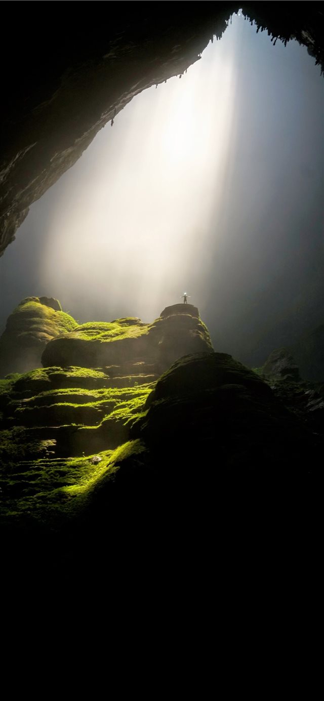 person on top of rock formation inside cave iPhone X wallpaper 