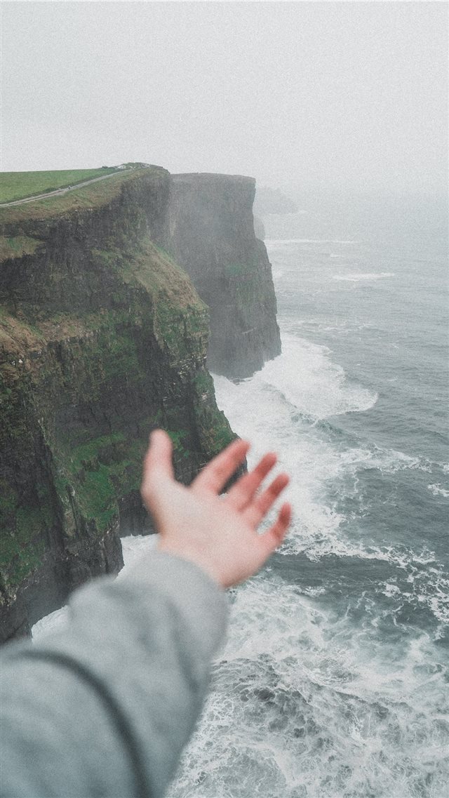 person standing on the cliff near the ocean iPhone 8 wallpaper 