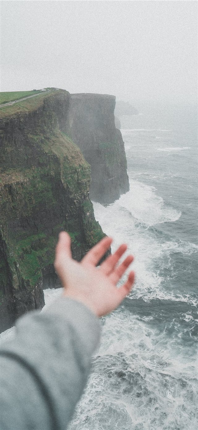 person standing on the cliff near the ocean iPhone X wallpaper 