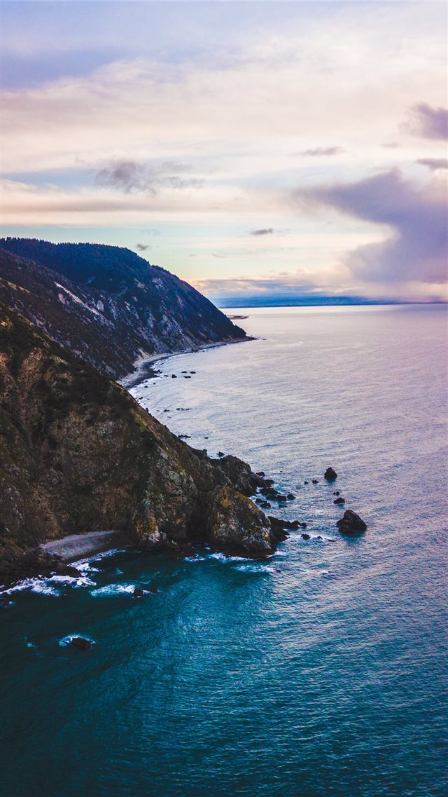 calm body of water crashing on shore of cliff unde... iPhone 8 wallpaper 