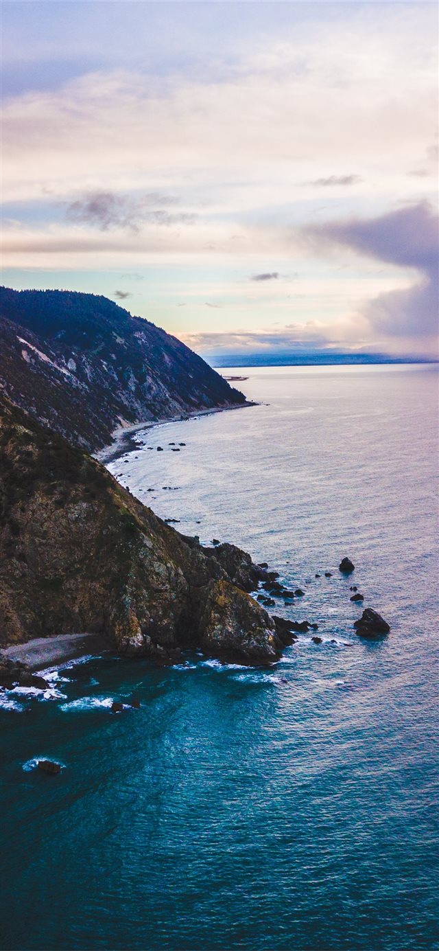 calm body of water crashing on shore of cliff unde... iPhone X wallpaper 