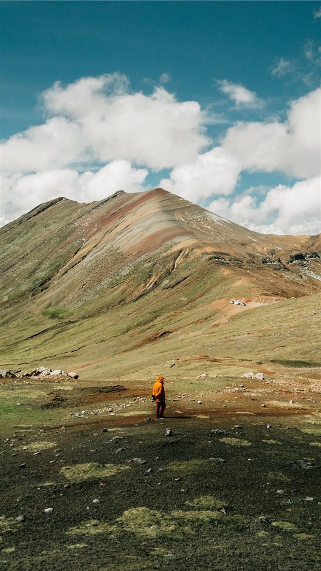 man standing on green grass field near mountain ri... iPhone 8 wallpaper 