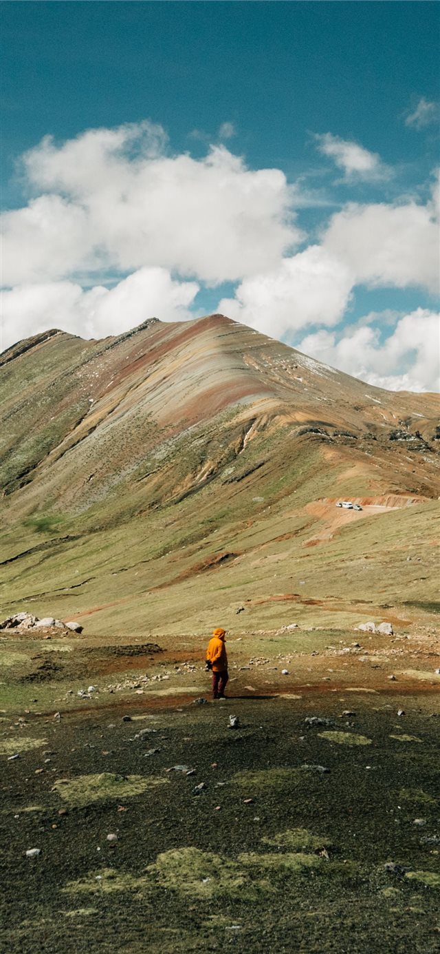man standing on green grass field near mountain ri... iPhone X wallpaper 