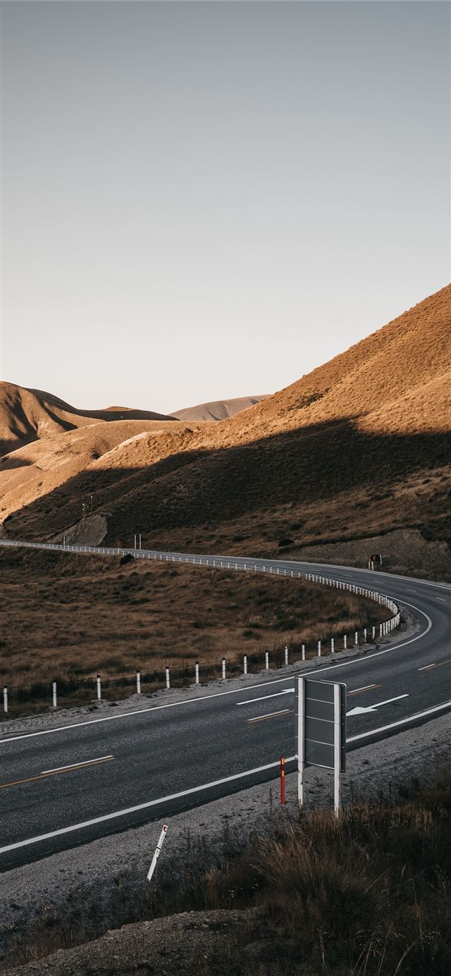gray asphalt road between brown mountains during d... iPhone X wallpaper 