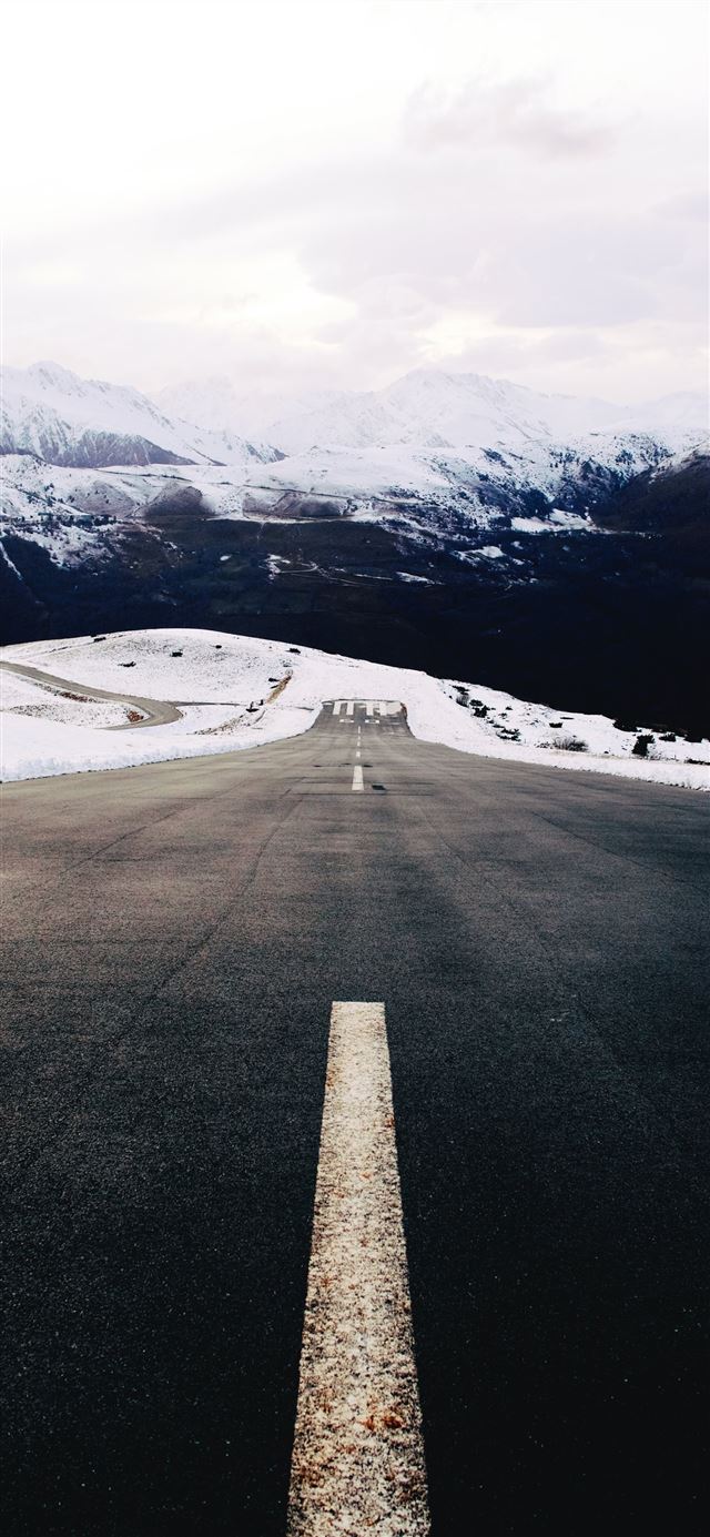 gray concrete road near snow covered mountain duri... iPhone X wallpaper 