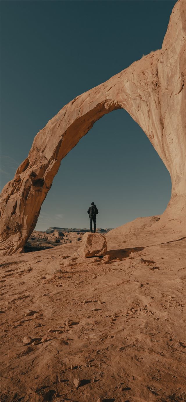 man in black jacket standing on brown rock formati... iPhone 11 wallpaper 