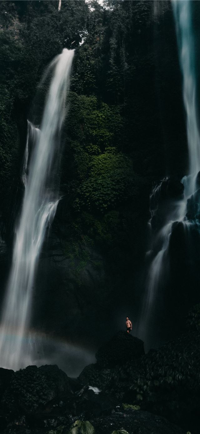 people sitting on rock in front of waterfalls duri... iPhone X wallpaper 