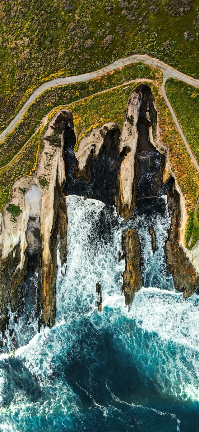 waves breaking on brown rock cliff in beach iPhone X wallpaper 