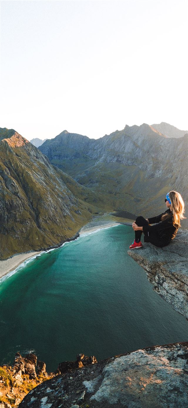woman sitting on cliff overlooking body of water n... iPhone 11 wallpaper 