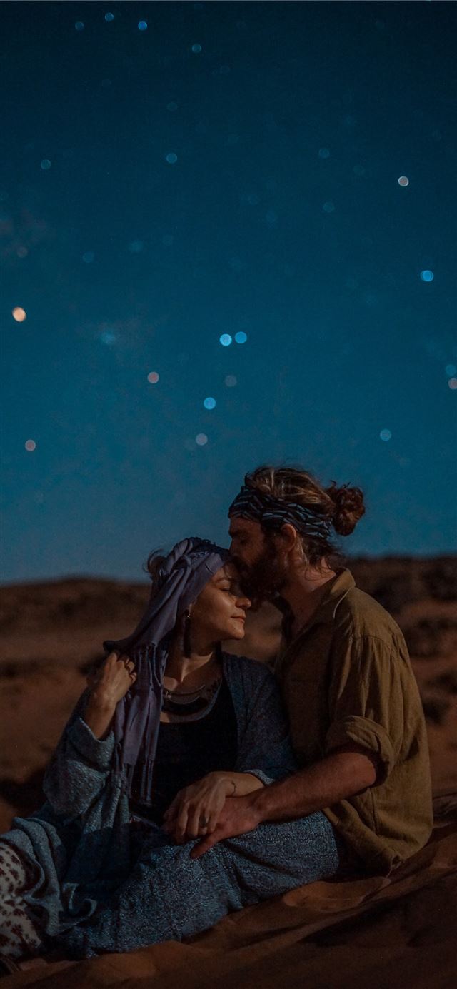 man and woman sitting on desert sand under blue sk... iPhone 11 wallpaper 