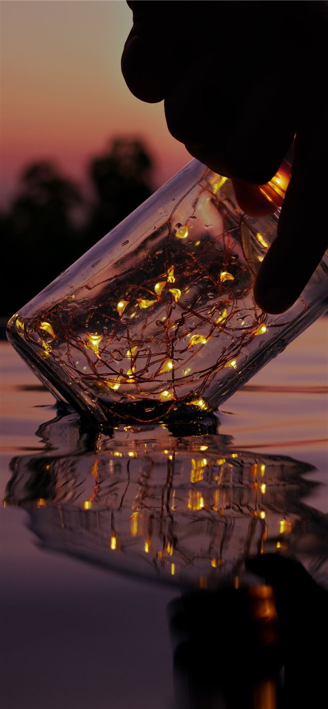 person holding string lights on clear glass jar ab... iPhone 11 wallpaper 