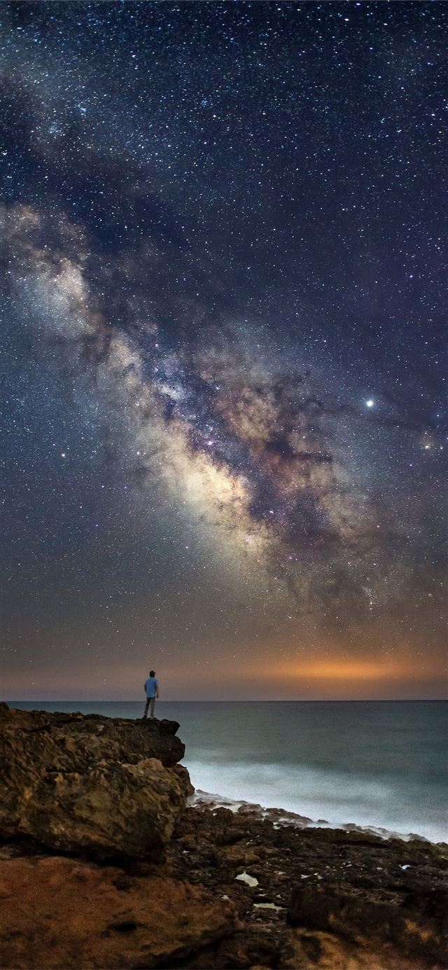 person standing on cliff during nighttime iPhone 11 wallpaper 