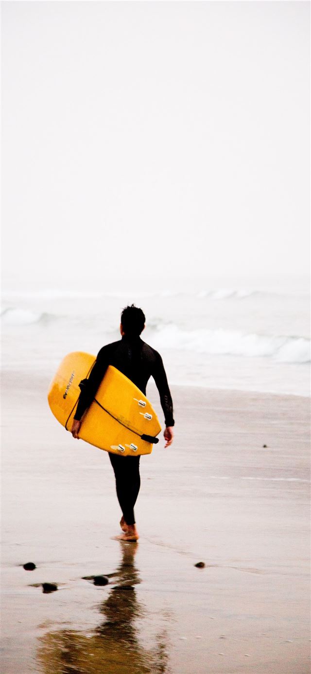 man holding yellow surfboard while walking on seas... iPhone 11 wallpaper 
