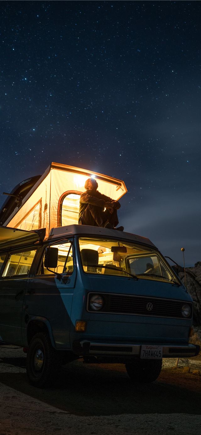 man sitting on top of blue van staring at sky duri... iPhone 8 wallpaper 