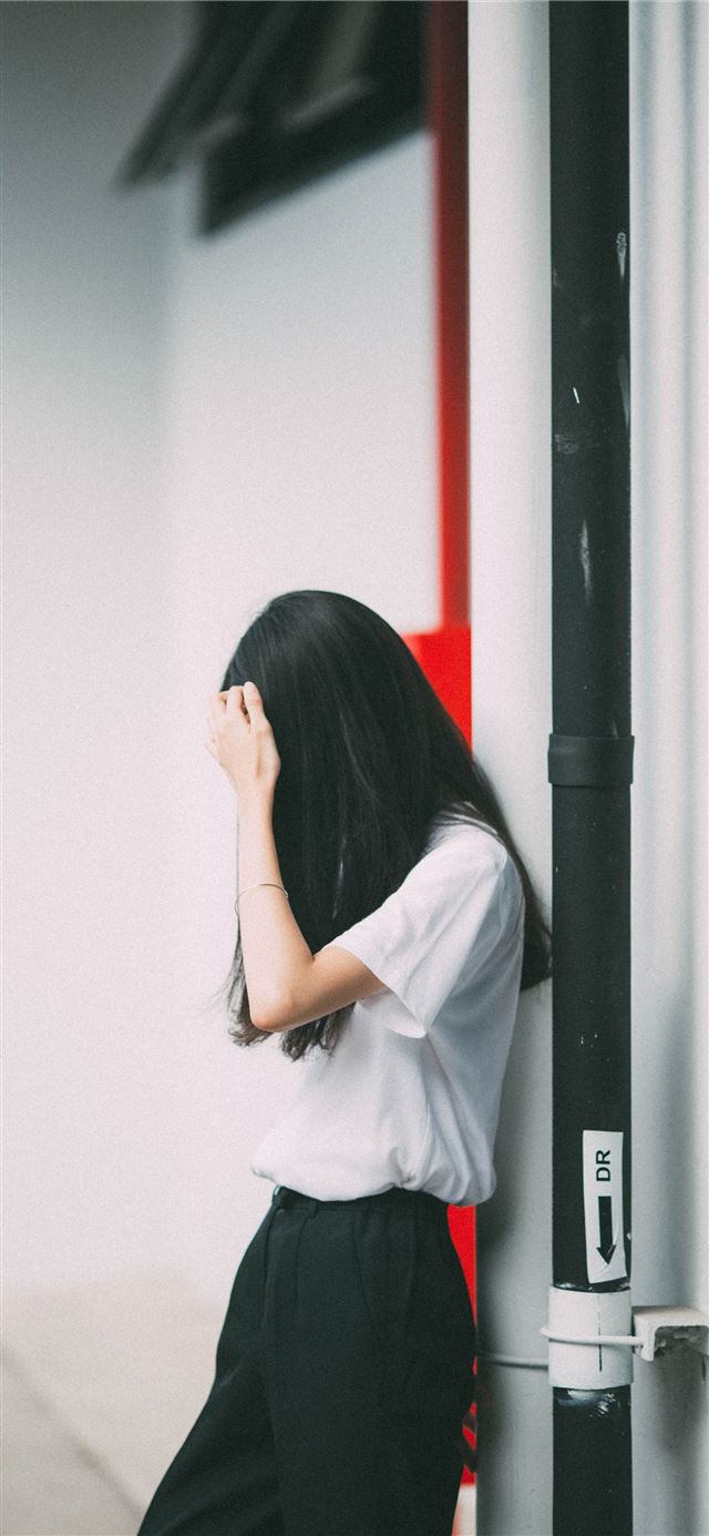 woman leaning on white concrete wall iPhone 11 wallpaper 