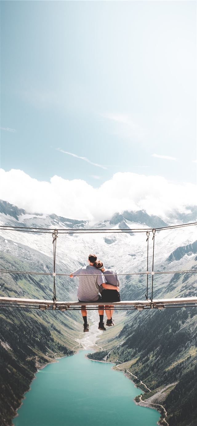 man and woman sitting on hanging bridge at daytime iPhone 11 wallpaper 